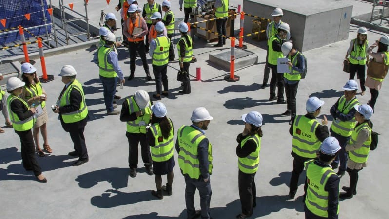Aerial view of a group of construction workers in hard hats and safety vests standing in a circle at a job site.