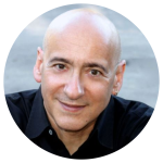 Close up headshot of Allan Rich, award nominated songwriter, smiling warmly at the camera with his arms folded and wearing a black button down shirt.