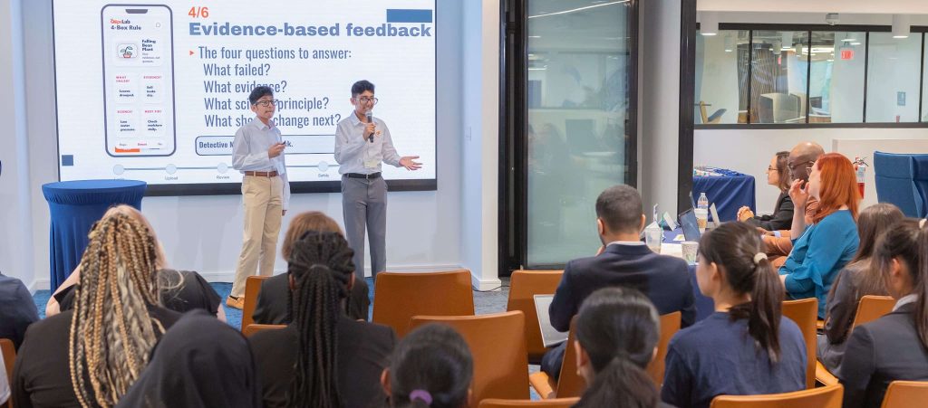 Two presenters discussing evidence-based feedback framework in front of an audience seated in a conference room.