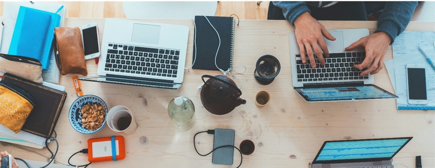 Aerial view of two laptops and work items on a desk with someone typing on their laptop