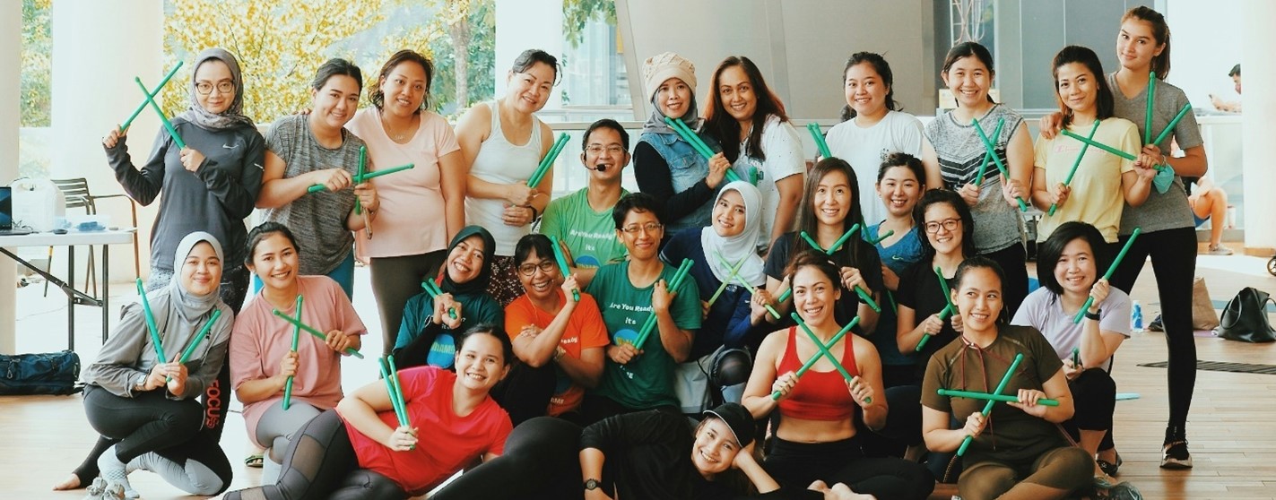 A group of company employees standing for group photo, all holding green drum sticks