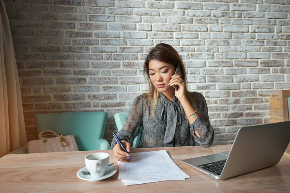 Businesswomen having serious conversation on cell telephone while sitting in front of open net-book